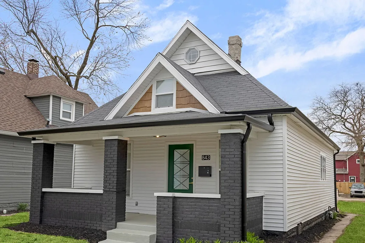 After the renovation. The same bungalow with fresh white siding, charcoal brick porch columns, a green front door, a new roof, and new landscaping.