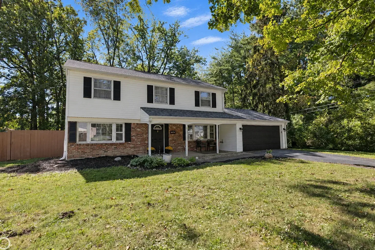 1629 W 74th Pl, a two story home with red brick on the first floor, white siding above, black shutters, a covered front porch, and an attached two car garage